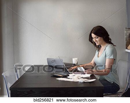 Stock Image - Caucasian woman holding receipt and using laptop. Fotosearch