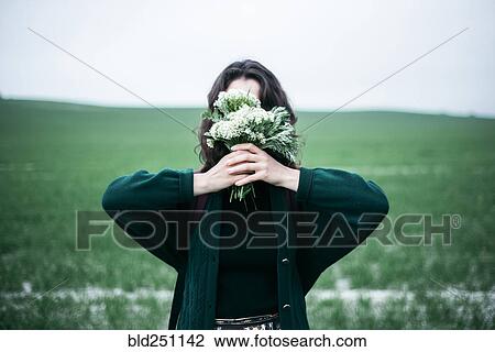 Stock Image - Caucasian woman holding wildflowers in front of face. Fotosearch