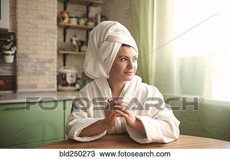 Stock Image - Caucasian woman in bathrobe and towel warming hands on cup. Fotosearch