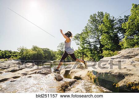 Stock Photo - Caucasian woman jumping on rocks near river. Fotosearch