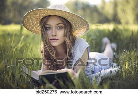 Stock Photograph - Caucasian woman laying in grass reading book. Fotosearch