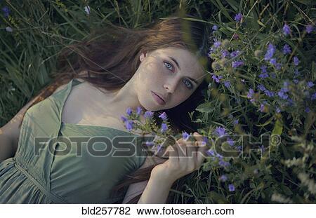 Stock Image - Caucasian woman laying in grass with wildflowers. Fotosearch