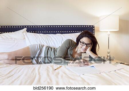 Caucasian woman laying on bed texting on cell phone View Large Photo Image Stock Image - Caucasian woman laying on bed texting on cell phone. Fotosearch