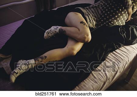 Stock Image - Caucasian woman laying on bed with tattoos on legs. Fotosearch