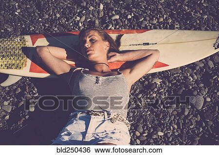 Stock Photograph - Caucasian woman laying on surfboard on beach. Fotosearch