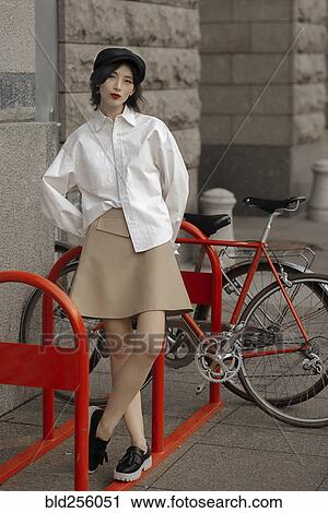 Stock Image - Caucasian woman leaning on bicycle rack. Fotosearch