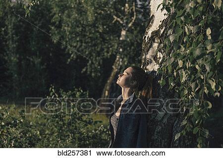 Stock Image - Caucasian woman leaning on tree trunk. Fotosearch