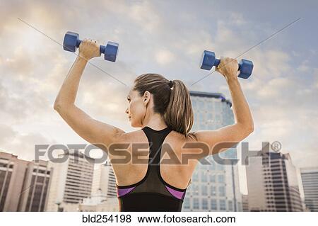 Stock Photo - Caucasian woman lifting dumbbells in city. Fotosearch