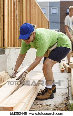 Stock Photo - Caucasian woman lifting lumber at construction site. Fotosearch