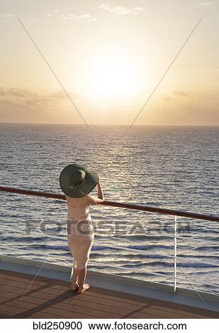 Stock Image - Caucasian woman on boat admiring sunset. Fotosearch