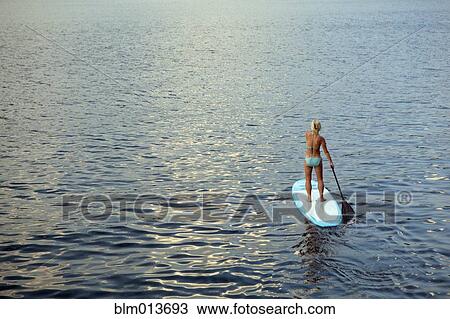 Stock Image - Caucasian woman on paddleboard on lake. Fotosearch