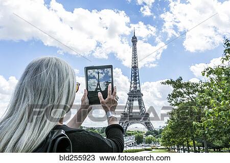 Stock Image - Caucasian woman photographing Eiffel Tower with digital tablet. Fotosearch