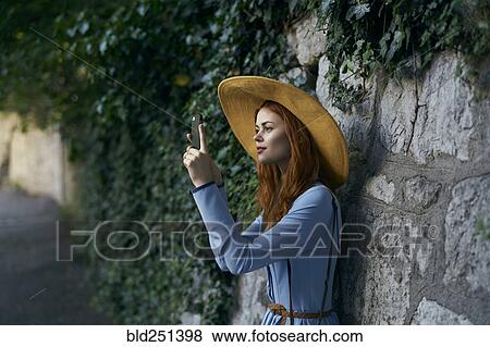 Stock Photo - Caucasian woman photographing with cell phone near stone wall. Fotosearch