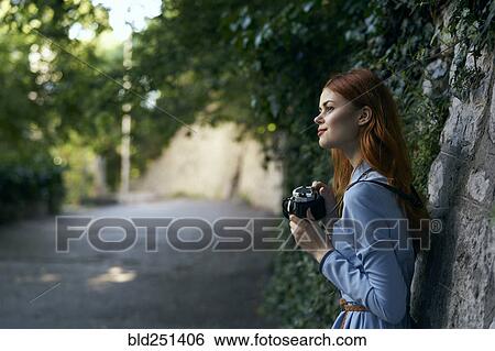 Stock Photograph - Caucasian woman photographing with camera near stone wall. Fotosearch