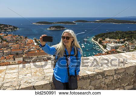 Stock Image - Caucasian woman posing for cell phone selfie with scenic view of ocean. Fotosearch