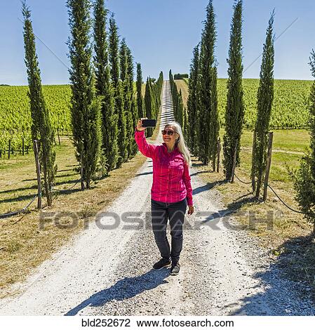 Stock Image - Caucasian woman posing for cell phone selfie on dirt road. Fotosearch