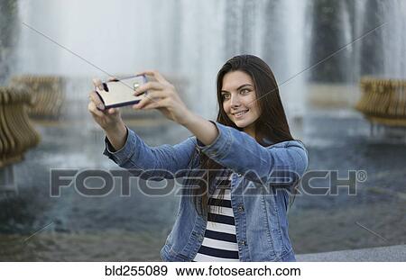 Stock Photo - Caucasian woman posing for cell phone selfie near fountain. Fotosearch