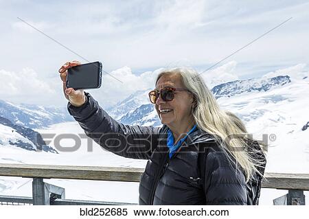 Stock Photography - Caucasian woman posing for cell phone selfie near snowy mountains. Fotosearch