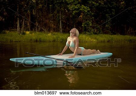 Stock Photo - Caucasian woman practicing yoga on paddleboard. Fotosearch