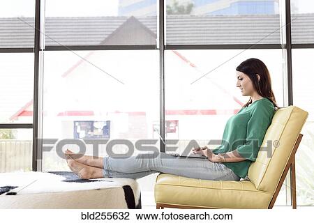 Stock Image - Caucasian woman relaxing and using laptop. Fotosearch