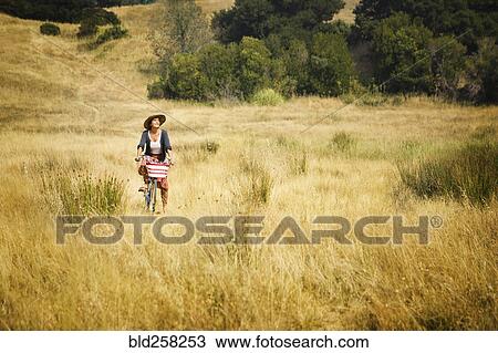 Stock Image - Caucasian woman riding bicycle in field. Fotosearch