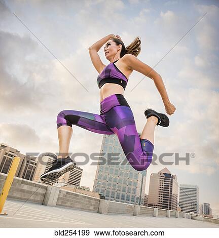 Stock Photo - Caucasian woman running and jumping on urban rooftop. Fotosearch