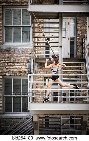 Stock Image - Caucasian woman running on urban staircase. Fotosearch