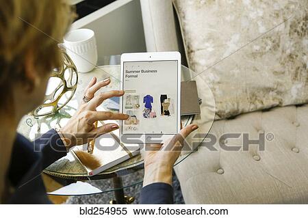 Stock Photography - Caucasian woman shopping for clothing on digital tablet. Fotosearch