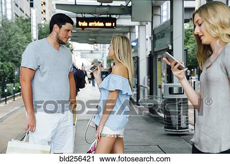 Stock Image - Caucasian woman showing cell phone to man at train station. Fotosearch