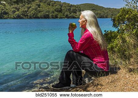 Caucasian woman sitting at lake eating apple View Large Photo Image Stock Photography - Caucasian woman sitting at lake eating apple. Fotosearch