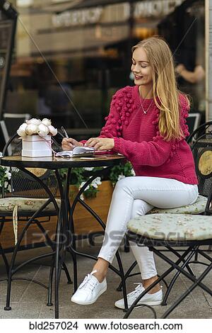 Picture - Caucasian woman sitting at table writing in journal. Fotosearch