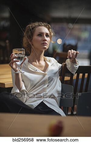 Stock Photo - Caucasian woman sitting at table drinking water. Fotosearch