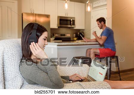 Caucasian woman sitting in armchair using laptop listening to headphones View Large Photo Image Stock Image - Caucasian woman sitting in armchair using laptop listening to headphones. Fotosearch