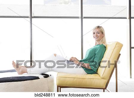 Stock Image - Caucasian woman sitting in chair using laptop. Fotosearch