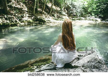 Stock Photo - Caucasian woman sitting near river. Fotosearch