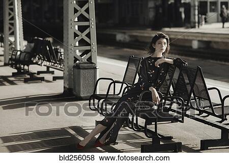Stock Photo - Caucasian woman sitting on bench at train station. Fotosearch