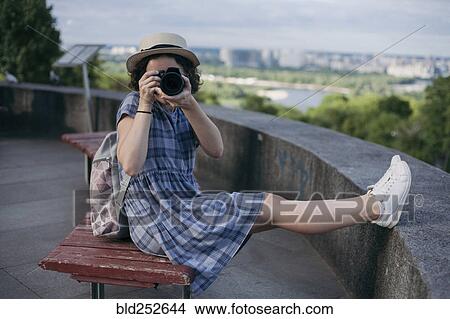 Picture - Caucasian woman sitting on bench photographing with camera. Fotosearch
