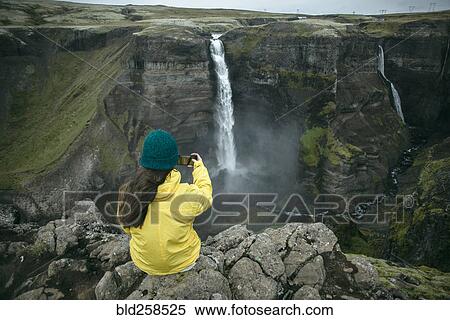 Caucasian woman sitting on cliff photographing waterfall View Large Photo Image Stock Photography - Caucasian woman sitting on cliff photographing waterfall. Fotosearch