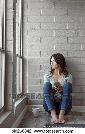 Stock Image - Caucasian woman sitting on floor texting on cell phone. Fotosearch