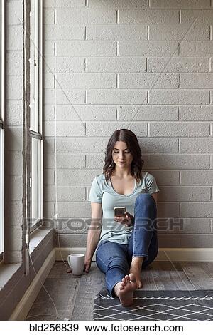 Stock Photo - Caucasian woman sitting on floor texting on cell phone. Fotosearch