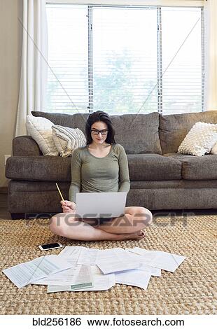 Stock Photograph - Caucasian woman sitting on floor using laptop near paperwork. Fotosearch