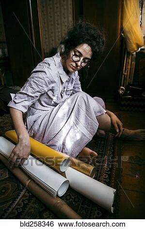 Stock Photograph - Caucasian woman sitting on floor with rolled up paper. Fotosearch