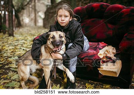 Stock Image - Caucasian woman sitting on sofa outdoors hugging dog. Fotosearch