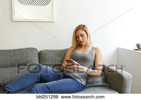 Stock Photo - Caucasian woman sitting on sofa texting on cell phone. Fotosearch