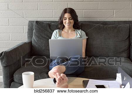 Caucasian woman sitting on sofa using laptop View Large Photo Image Stock Photo - Caucasian woman sitting on sofa using laptop. Fotosearch