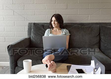 Stock Photo - Caucasian woman sitting on sofa using laptop. Fotosearch
