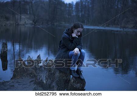 Stock Photography - Caucasian woman sitting on tree stump near river thinking. Fotosearch
