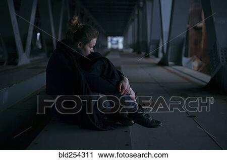 Stock Image - Caucasian woman sitting under bridge. Fotosearch