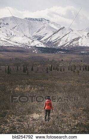 Stock Image - Caucasian woman standing in field near snowy mountain. Fotosearch