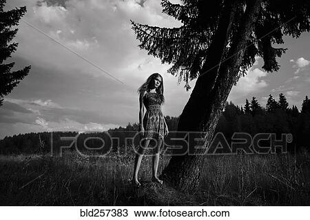 Stock Image - Caucasian woman standing in field near tree. Fotosearch